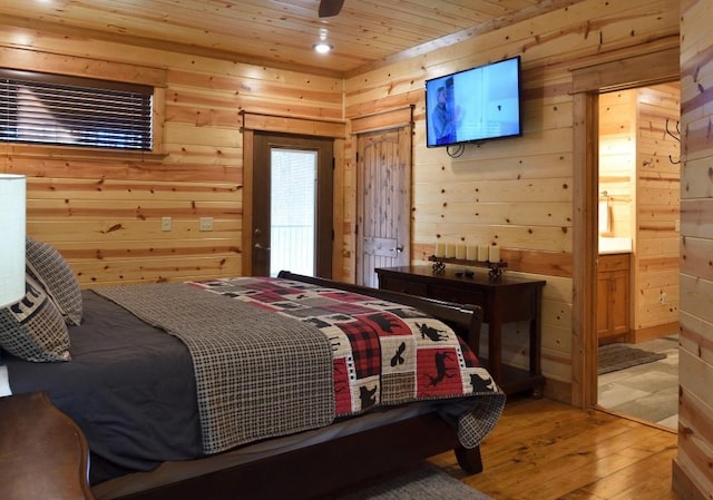 bedroom with wood-type flooring, ensuite bathroom, and wooden walls