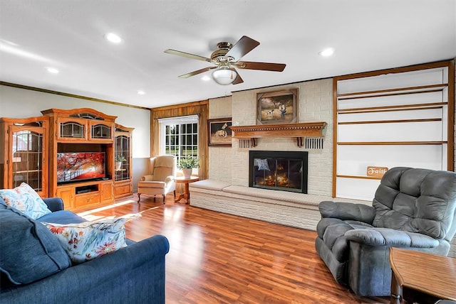 living room featuring hardwood / wood-style flooring, a brick fireplace, ceiling fan, and crown molding