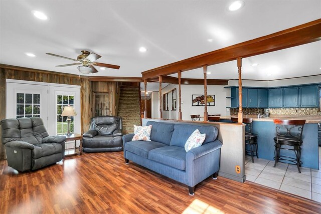 living room with hardwood / wood-style floors, ceiling fan, wood walls, and beam ceiling