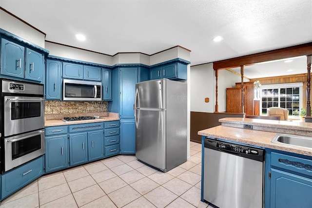 kitchen with blue cabinetry, sink, stainless steel appliances, backsplash, and light tile patterned flooring