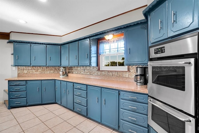 kitchen featuring backsplash, blue cabinets, light tile patterned floors, ornamental molding, and stainless steel double oven