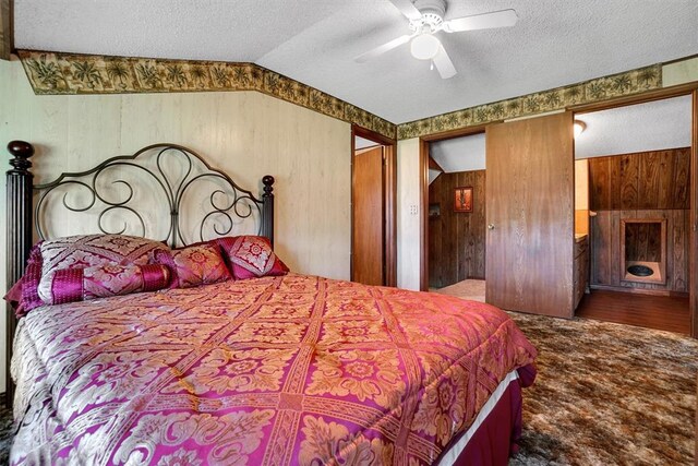 bedroom featuring ceiling fan, wood walls, hardwood / wood-style floors, a textured ceiling, and vaulted ceiling