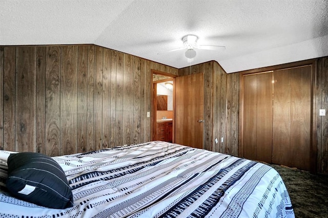 bedroom with ceiling fan, wood walls, a textured ceiling, lofted ceiling, and a closet