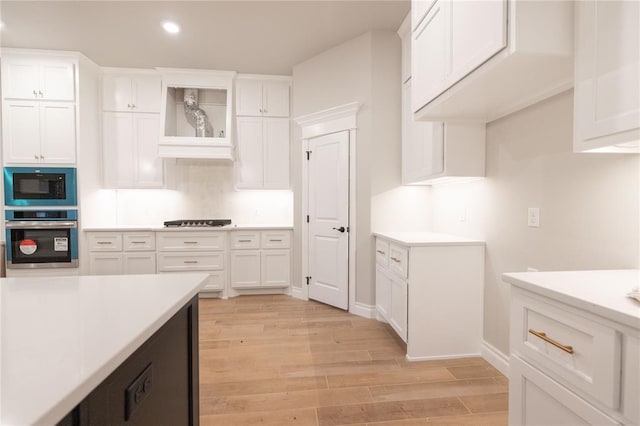 kitchen with cooktop, built in microwave, light countertops, light wood-type flooring, and stainless steel oven