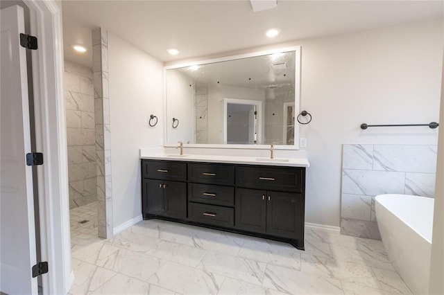 bathroom featuring marble finish floor, double vanity, recessed lighting, a freestanding bath, and a sink