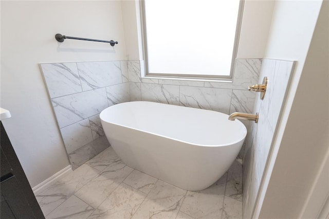 bathroom featuring a wainscoted wall, marble finish floor, and a soaking tub