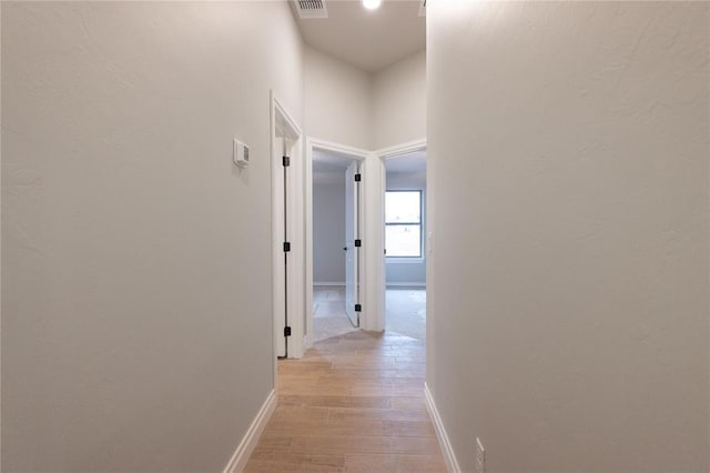 hallway featuring baseboards, visible vents, and light wood finished floors