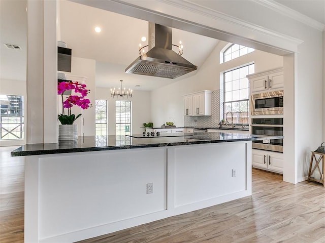 kitchen featuring appliances with stainless steel finishes, dark stone countertops, white cabinets, light hardwood / wood-style floors, and range hood