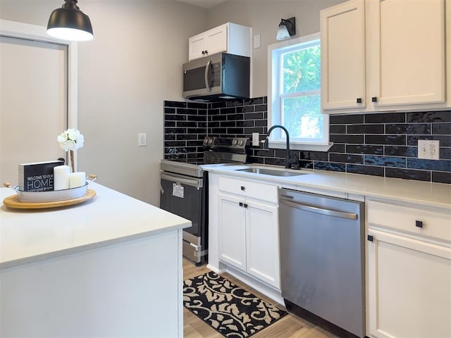 kitchen featuring white cabinets, hanging light fixtures, sink, appliances with stainless steel finishes, and light hardwood / wood-style floors