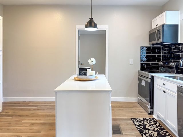 kitchen with tasteful backsplash, stainless steel appliances, light hardwood / wood-style floors, white cabinetry, and hanging light fixtures