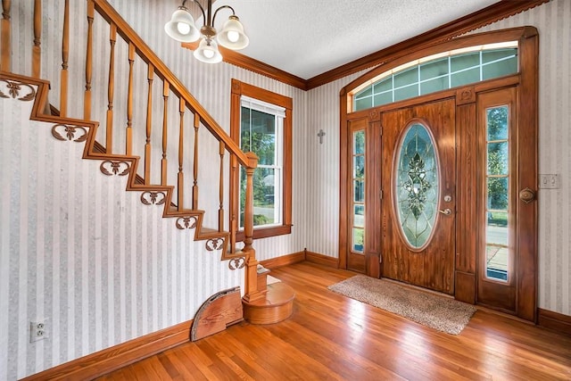 entrance foyer with a notable chandelier, ornamental molding, a textured ceiling, and hardwood / wood-style flooring