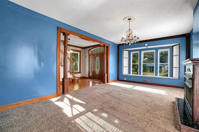 foyer entrance with carpet flooring, ornamental molding, a textured ceiling, and an inviting chandelier