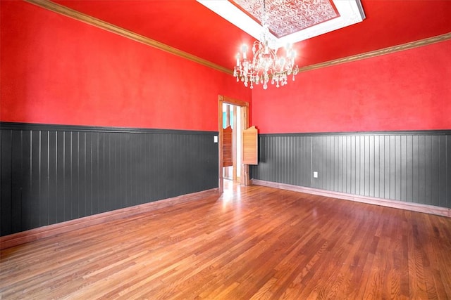 spare room featuring hardwood / wood-style floors, wood walls, an inviting chandelier, a skylight, and ornamental molding