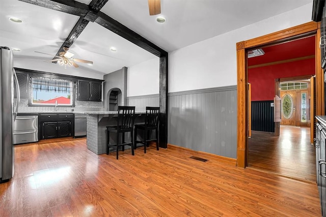 kitchen with sink, stainless steel appliances, tasteful backsplash, wood-type flooring, and a kitchen bar