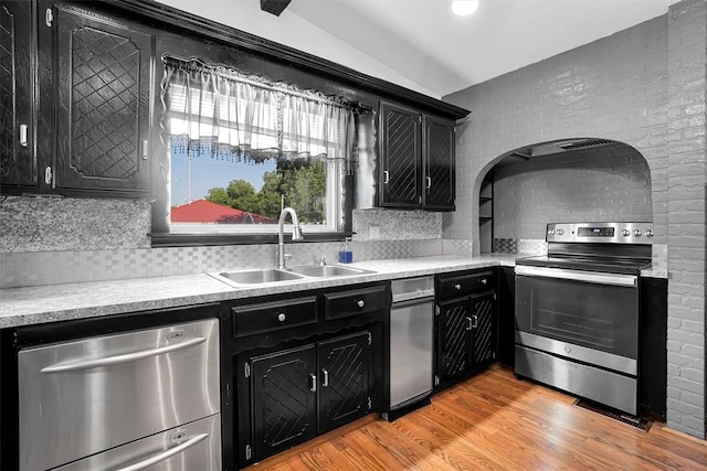 kitchen featuring lofted ceiling, sink, light hardwood / wood-style flooring, tasteful backsplash, and stainless steel appliances