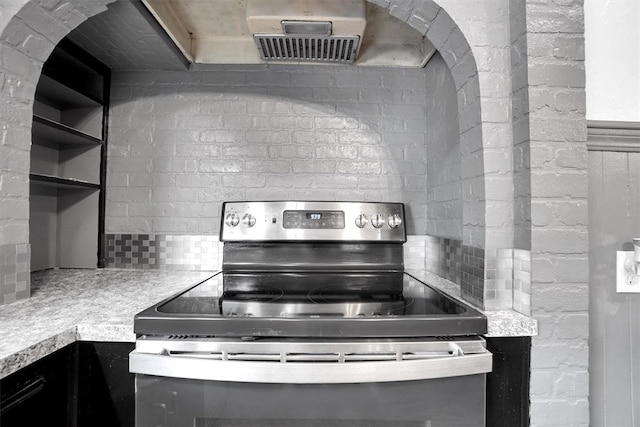 kitchen with stainless steel range with electric stovetop, brick wall, and range hood