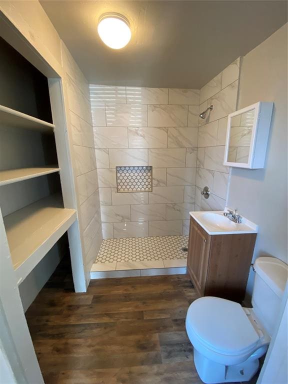 bathroom featuring toilet, wood-type flooring, vanity, and a tile shower