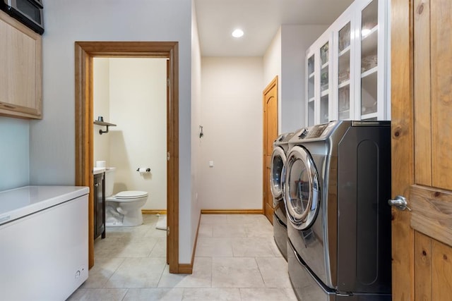 clothes washing area with washer and clothes dryer, cabinets, and light tile patterned floors