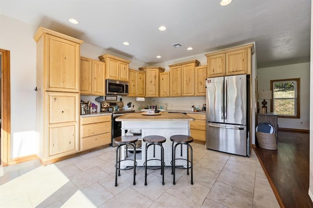 kitchen featuring a kitchen bar, light brown cabinetry, stainless steel appliances, and light hardwood / wood-style floors