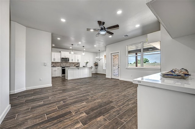 kitchen featuring dark wood-type flooring, hanging light fixtures, stainless steel appliances, white cabinets, and ceiling fan with notable chandelier