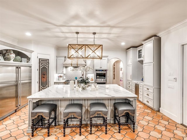 kitchen with decorative backsplash, appliances with stainless steel finishes, a large island with sink, decorative light fixtures, and a breakfast bar area