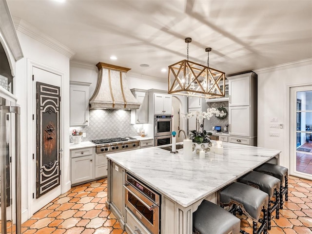 kitchen with custom exhaust hood, a kitchen island with sink, hanging light fixtures, appliances with stainless steel finishes, and a breakfast bar area