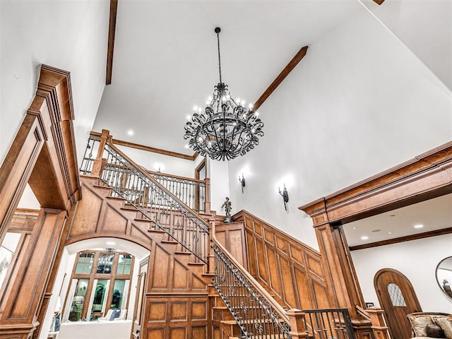 stairway featuring decorative columns, crown molding, a high ceiling, and an inviting chandelier