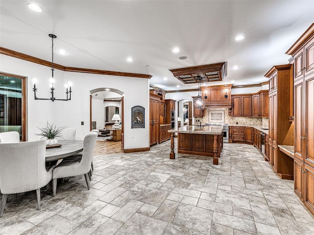 kitchen featuring tasteful backsplash, light stone counters, a kitchen island with sink, crown molding, and decorative light fixtures