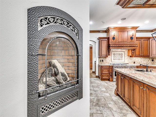 kitchen with decorative backsplash, light stone counters, ornamental molding, and stainless steel range