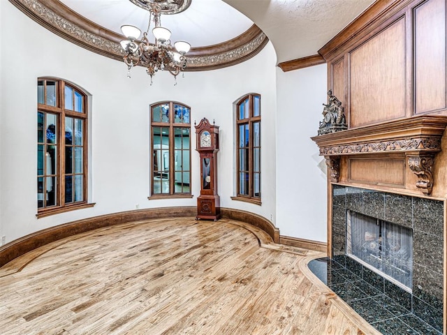 interior space with a high ceiling, a notable chandelier, crown molding, a tiled fireplace, and hardwood / wood-style flooring