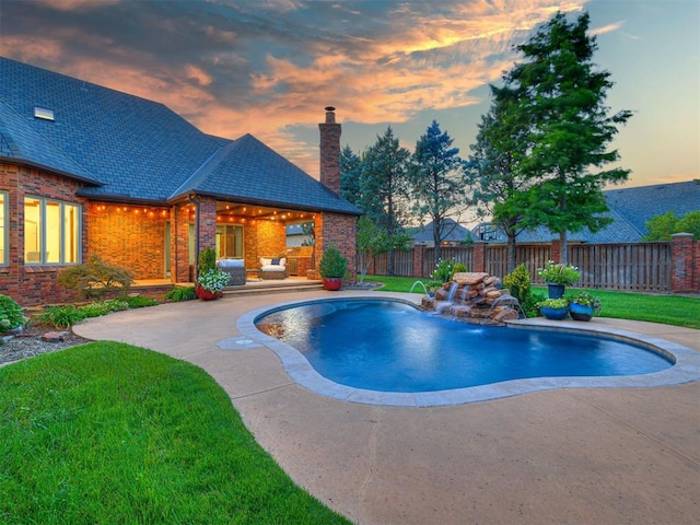 pool at dusk with pool water feature, a patio area, and a yard