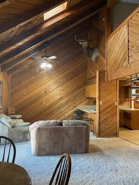 unfurnished living room featuring a skylight, ceiling fan, wooden ceiling, beamed ceiling, and wooden walls