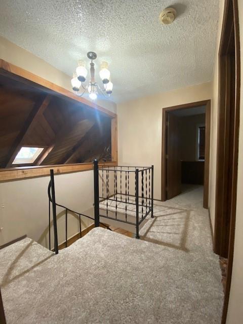 corridor with a skylight, light carpet, a textured ceiling, and a notable chandelier