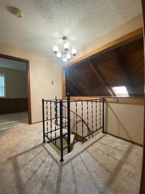 stairs with carpet flooring, wood walls, a textured ceiling, and an inviting chandelier