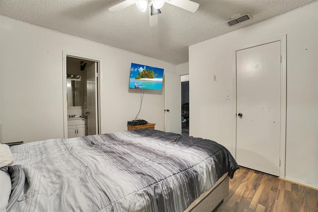 bedroom with a textured ceiling, connected bathroom, ceiling fan, and dark wood-type flooring