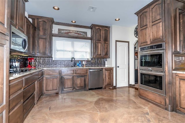 kitchen with backsplash, sink, light stone countertops, appliances with stainless steel finishes, and dark brown cabinetry