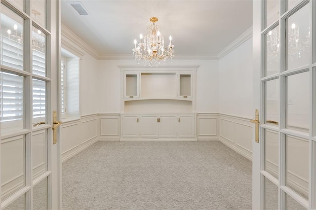 empty room with light carpet, crown molding, and a notable chandelier