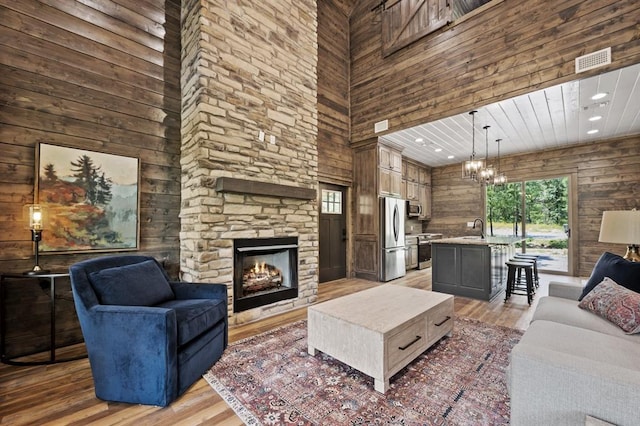 living room with a high ceiling, an inviting chandelier, sink, a fireplace, and wood-type flooring