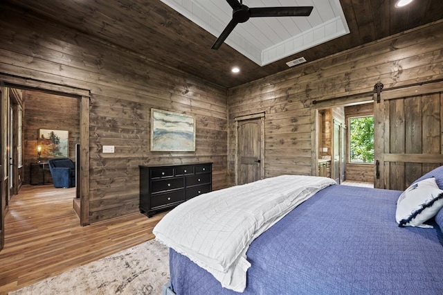 bedroom featuring wood ceiling, ceiling fan, wooden walls, wood-type flooring, and a barn door