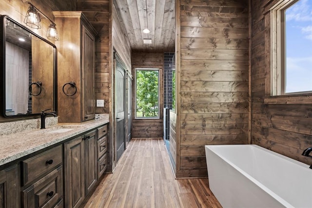 bathroom with a tub, wood walls, hardwood / wood-style floors, and vanity