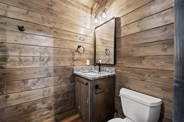 bathroom with vanity, toilet, and wooden walls