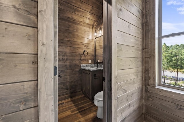 bathroom featuring wooden walls, hardwood / wood-style floors, vanity, and toilet