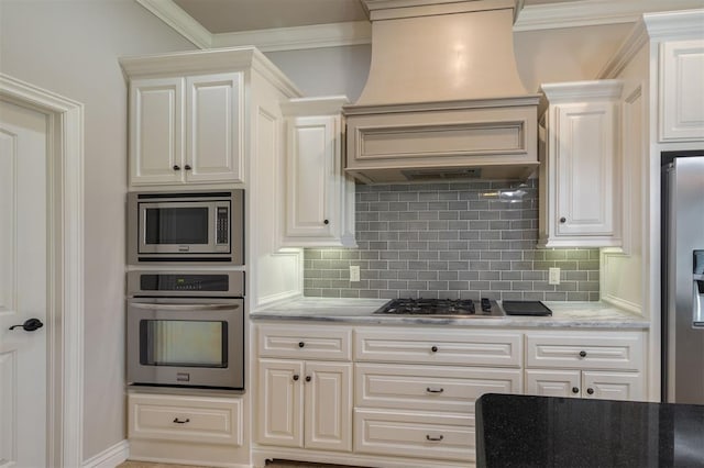 kitchen featuring light stone counters, decorative backsplash, white cabinets, custom range hood, and appliances with stainless steel finishes