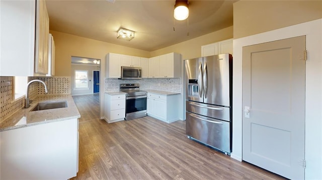 kitchen featuring backsplash, white cabinets, sink, light wood-type flooring, and appliances with stainless steel finishes