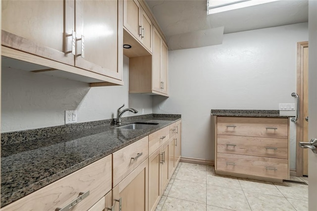 kitchen with light brown cabinetry, light tile patterned floors, dark stone countertops, and sink