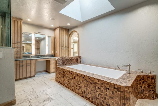 bathroom featuring a skylight, vanity, and a relaxing tiled tub