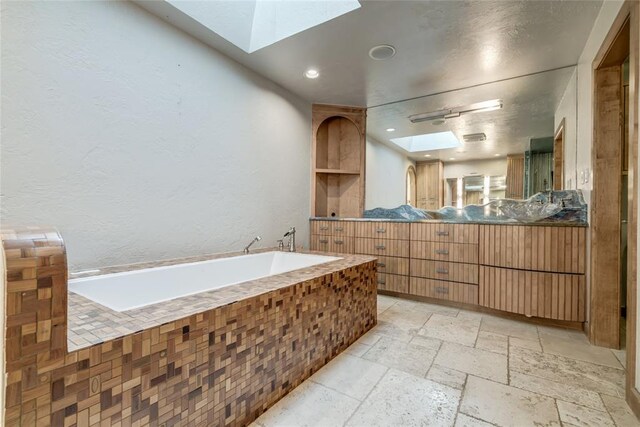 bathroom with a tub to relax in, vanity, and a skylight