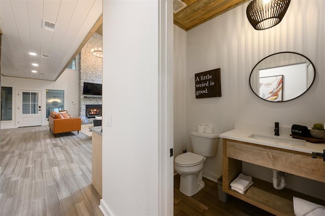 bathroom with sink, wood-type flooring, toilet, a fireplace, and wood ceiling