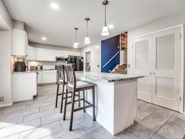 kitchen with pendant lighting, black refrigerator with ice dispenser, white cabinets, a kitchen island, and light stone counters