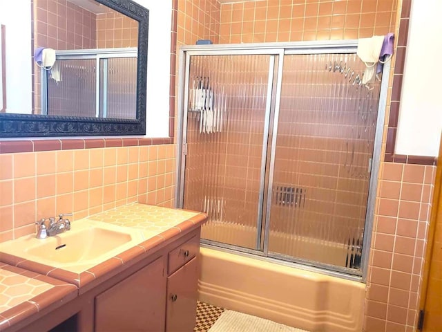 bathroom with vanity, tile walls, and bath / shower combo with glass door